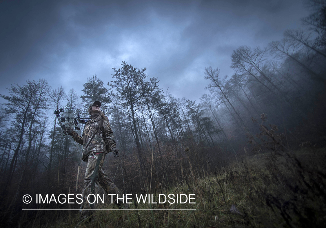 Woman bowhunting in fall forest.