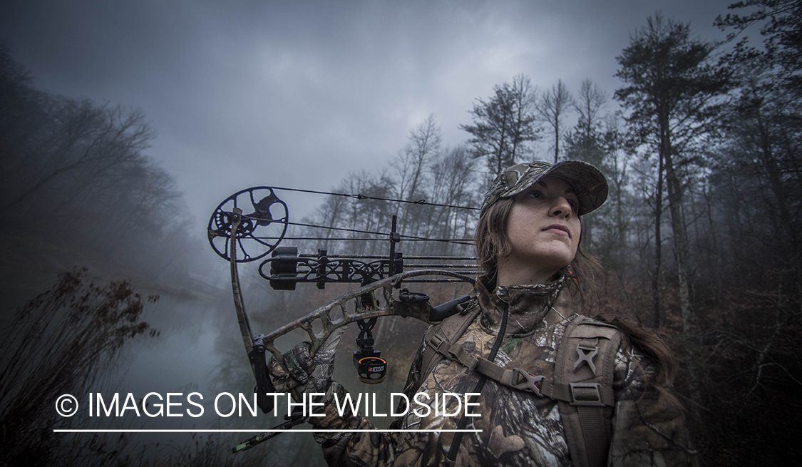Woman bowhunting in fall forest.