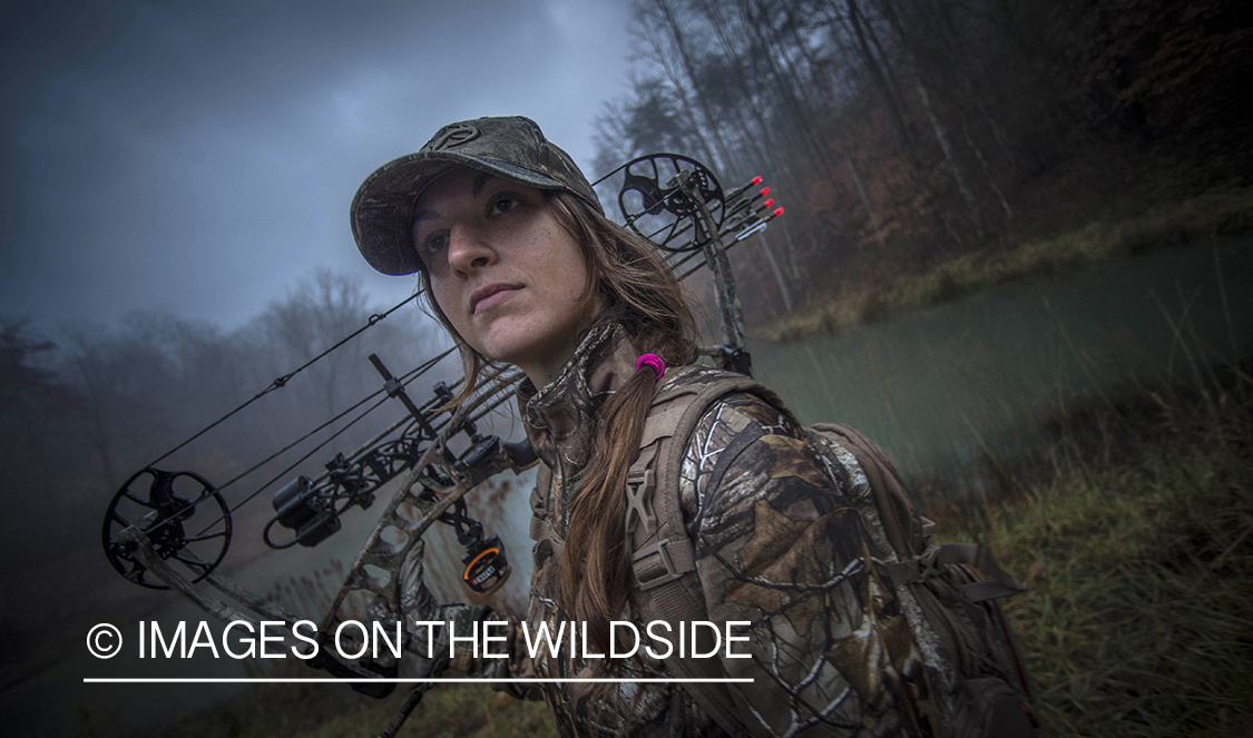 Woman bowhunting in fall forest.