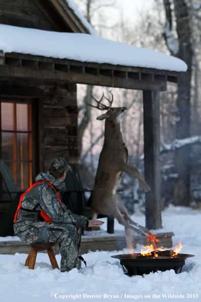 White-tailed deer hunter warming hands by campfire.