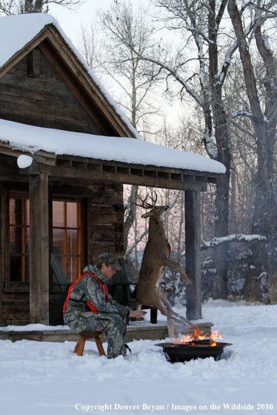 White-tailed deer hunter warming hands by campfire.