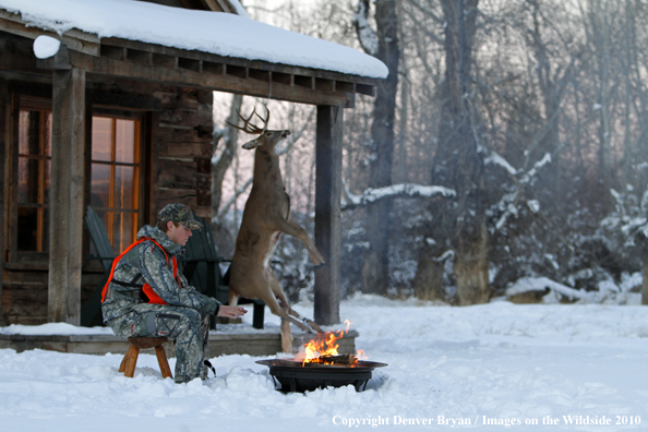 White-tailed deer hunter warming hands by campfire.