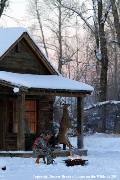 White-tailed deer hunter warming hands by campfire.