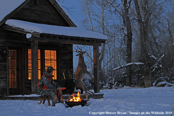White-tailed deer hunter warming hands by campfire.