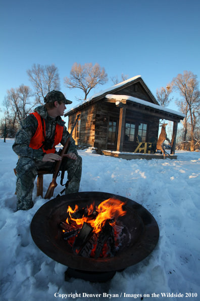White-tailed deer hunter warming hands by campfire.