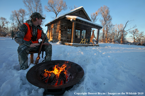 White-tailed deer hunter warming hands by campfire.