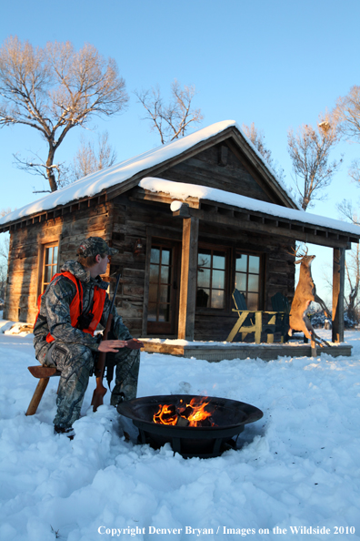 White-tailed deer hunter warming hands by campfire.
