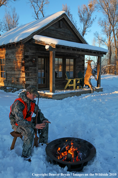 White-tailed deer hunter warming hands by campfire.