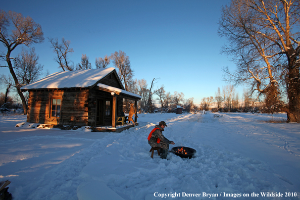 White-tailed deer hunter warming hands by campfire.