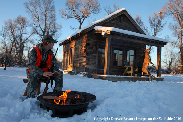 White-tailed deer hunter warming hands by campfire.