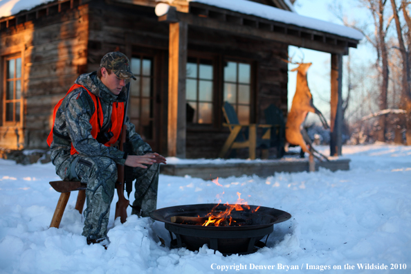 White-tailed deer hunter warming hands by campfire.