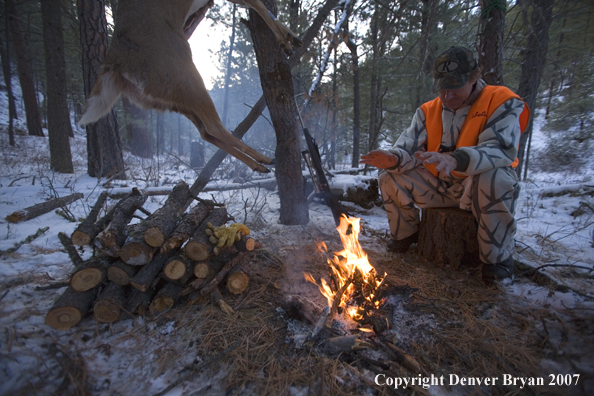 Hunter sitting around campfire with bagged white-tailed deer hanging from tree