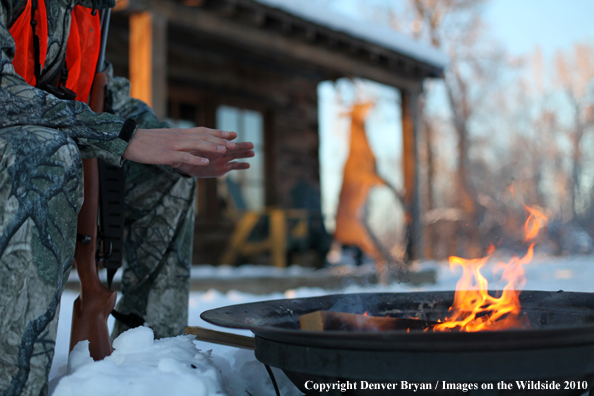 White-tailed deer hunter warming hands by campfire.