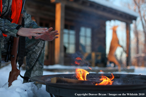 White-tailed deer hunter warming hands by campfire.