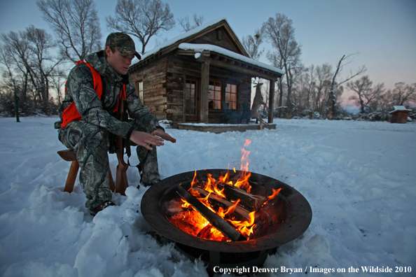 White-tailed deer hunter warming hands by campfire.