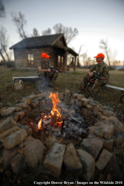 Hunters sitting around campfire in front of an old hunting shack where a white-tailed deer hangs. (Original image # 11024-049.89D)