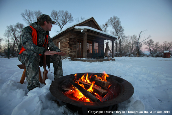 White-tailed deer hunter warming hands by campfire.