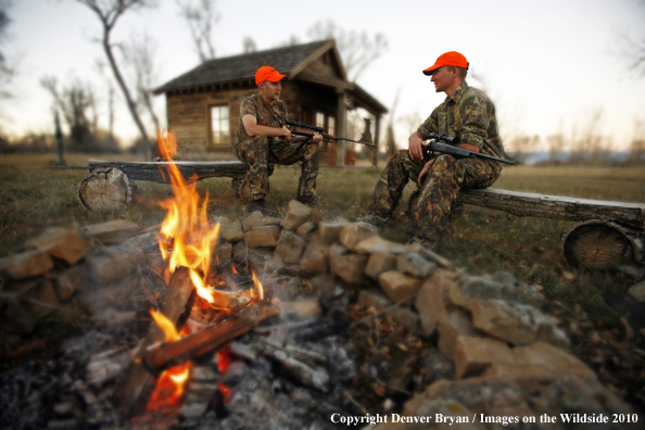 Hunters sitting around campfire in front of an old hunting shack where a white-tailed deer hangs. (Original image # 11024-050.16D)