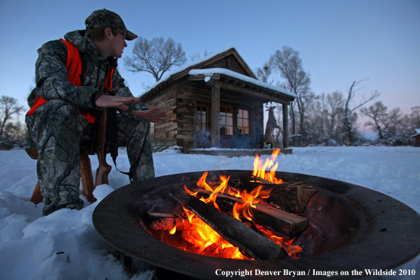 White-tailed deer hunter warming hands by campfire.