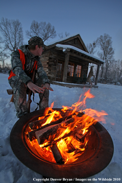 White-tailed deer hunter warming hands by campfire.