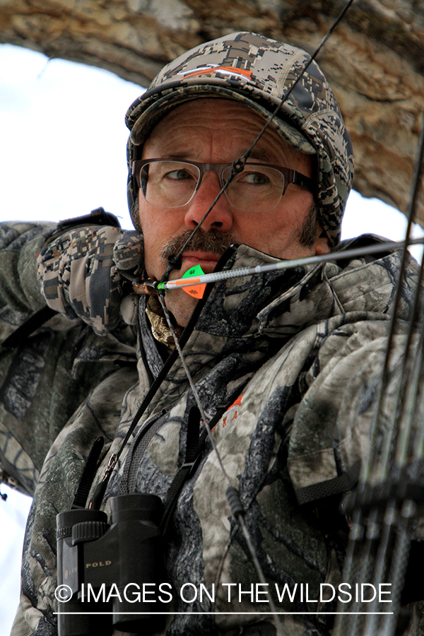 Bowhunter in tree stand taking aim. 
