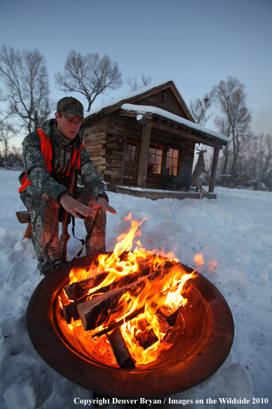 White-tailed deer hunter warming hands by campfire.