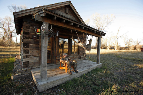 Archery hunter sittting on porch of old hunting shack where bagged white-tail hangs
