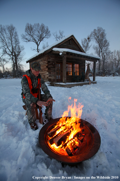 White-tailed deer hunter warming hands by campfire.