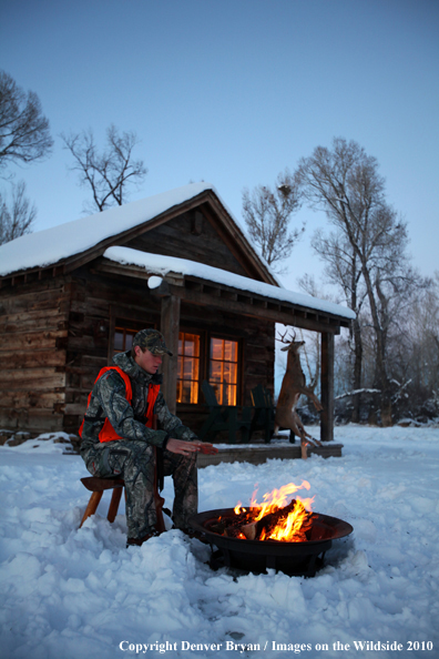 White-tailed deer hunter warming hands by campfire.