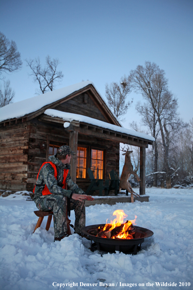 White-tailed deer hunter warming hands by campfire.