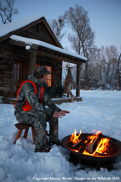 White-tailed deer hunter warming hands by campfire.