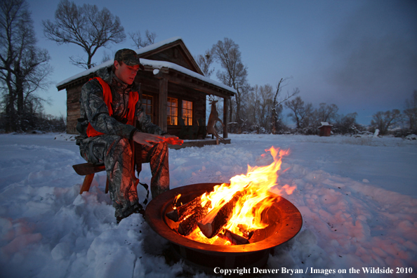 White-tailed deer hunter warming hands by campfire.