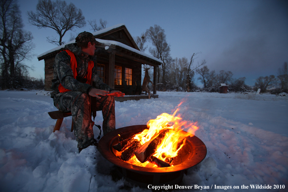 White-tailed deer hunter warming hands by campfire.