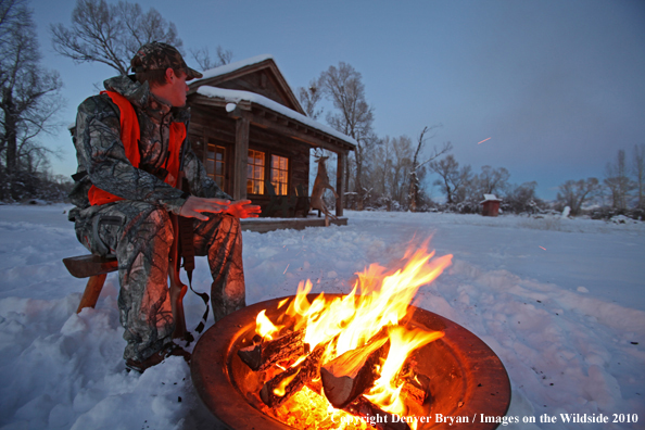 White-tailed deer hunter warming hands by campfire.